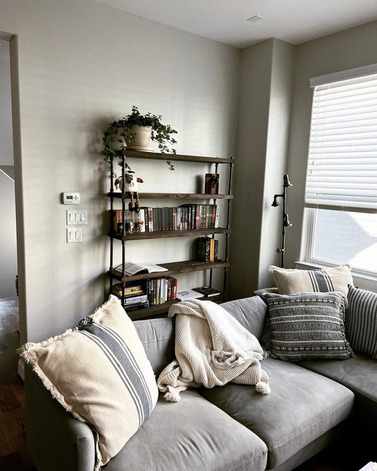 Etagere bookcase made of wood and black iron pipe, behind a couch with fluffy pillows.