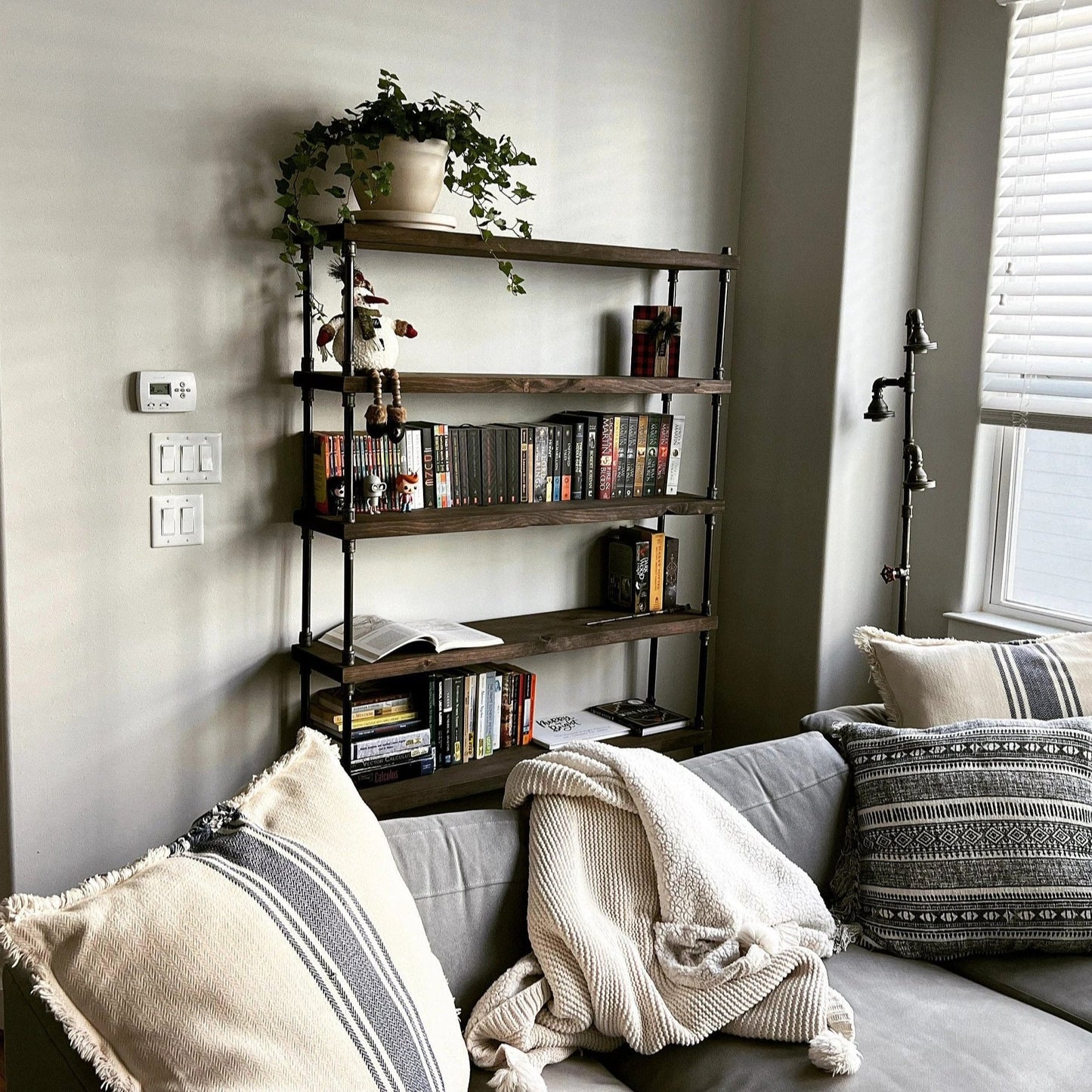 HANDMADE INDUSTRIAL BOOKCASE 6 SHELF, DARK BROWN STAIN COLOR WOOD SHELVES WITH IRON PIPE SIDERAILS, GRAY SOFA WITH DECORATIVE PILLOWS IN FOREGROUND