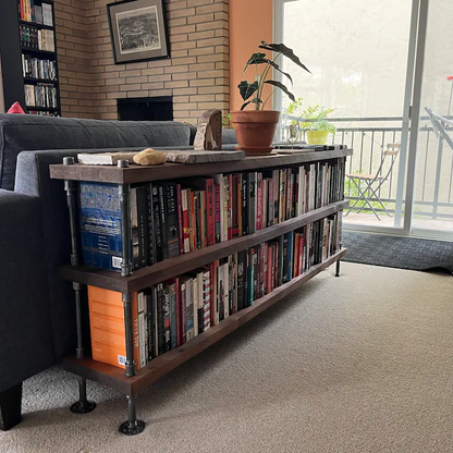 Bookcase unit with 3 shelves, 72 inches ling and 34 inches in hieght. Shelving unit is behind a dark blue sofa in a bright room with modern farmhouse decor style. Shelving unit has books lined up from end to end.