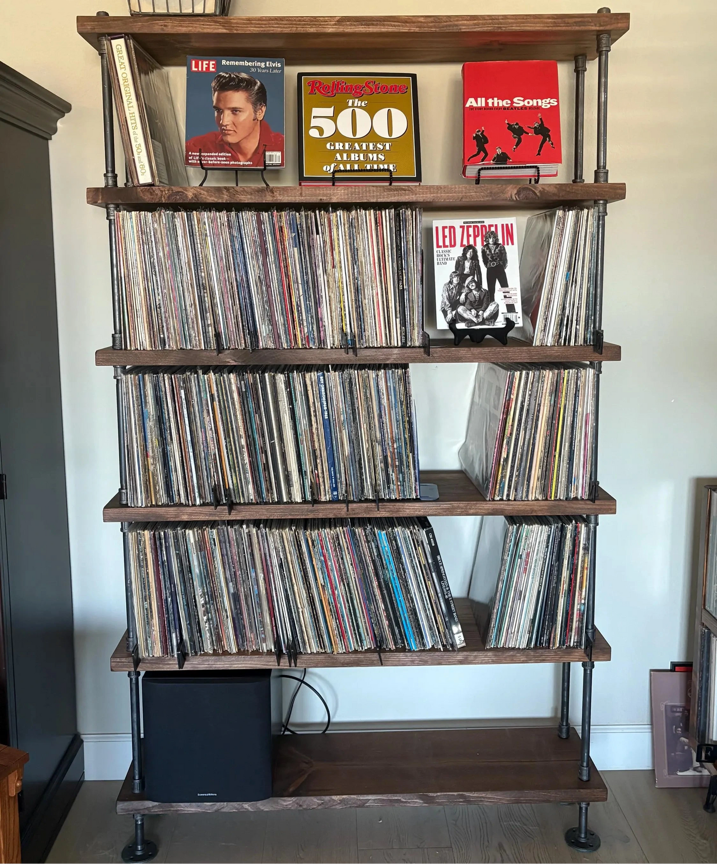 Wooden record shelf with vinyl records and album covers on a white wall.