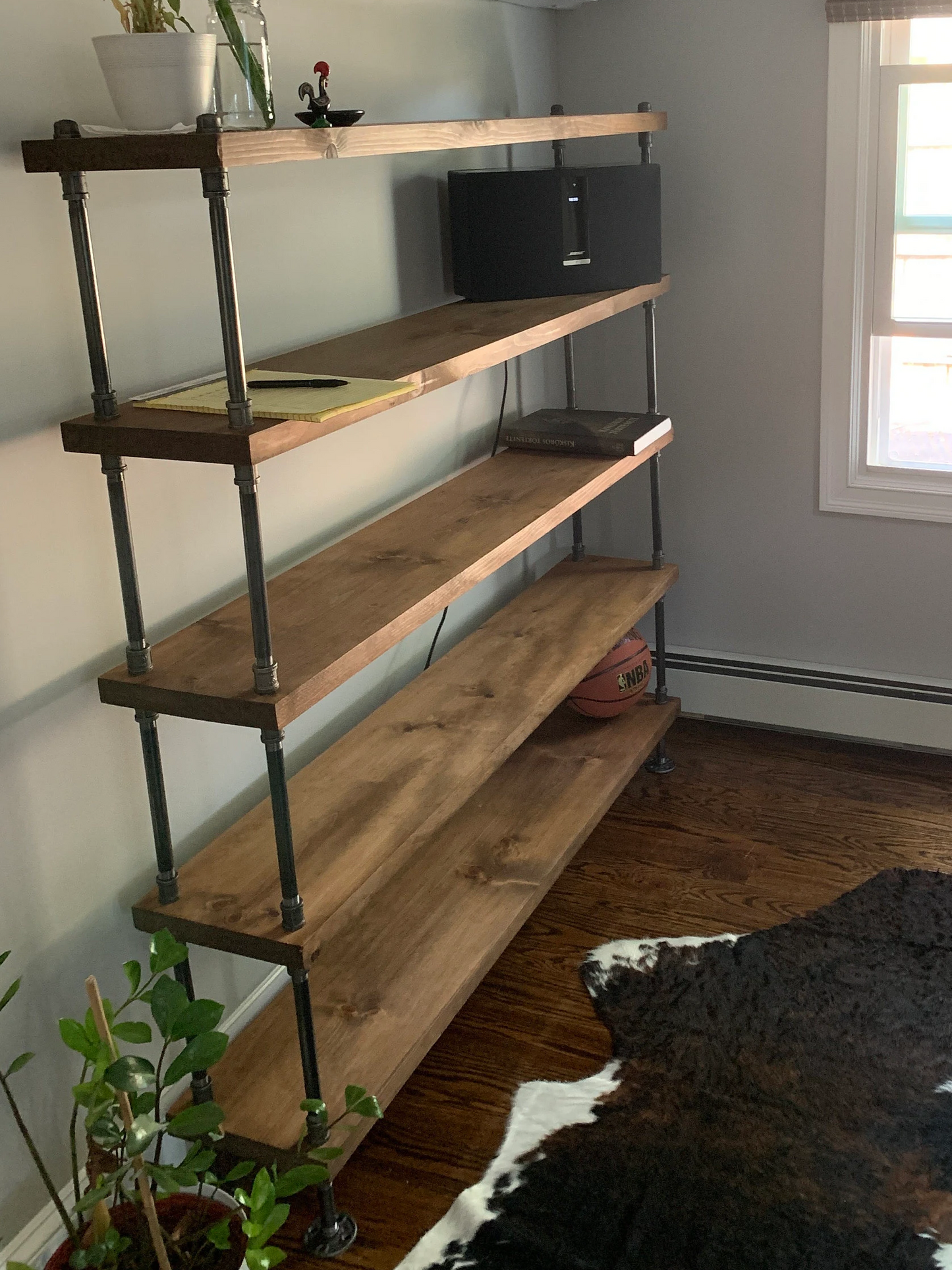 Wooden shelf with plants in a room with a window and air conditioner.